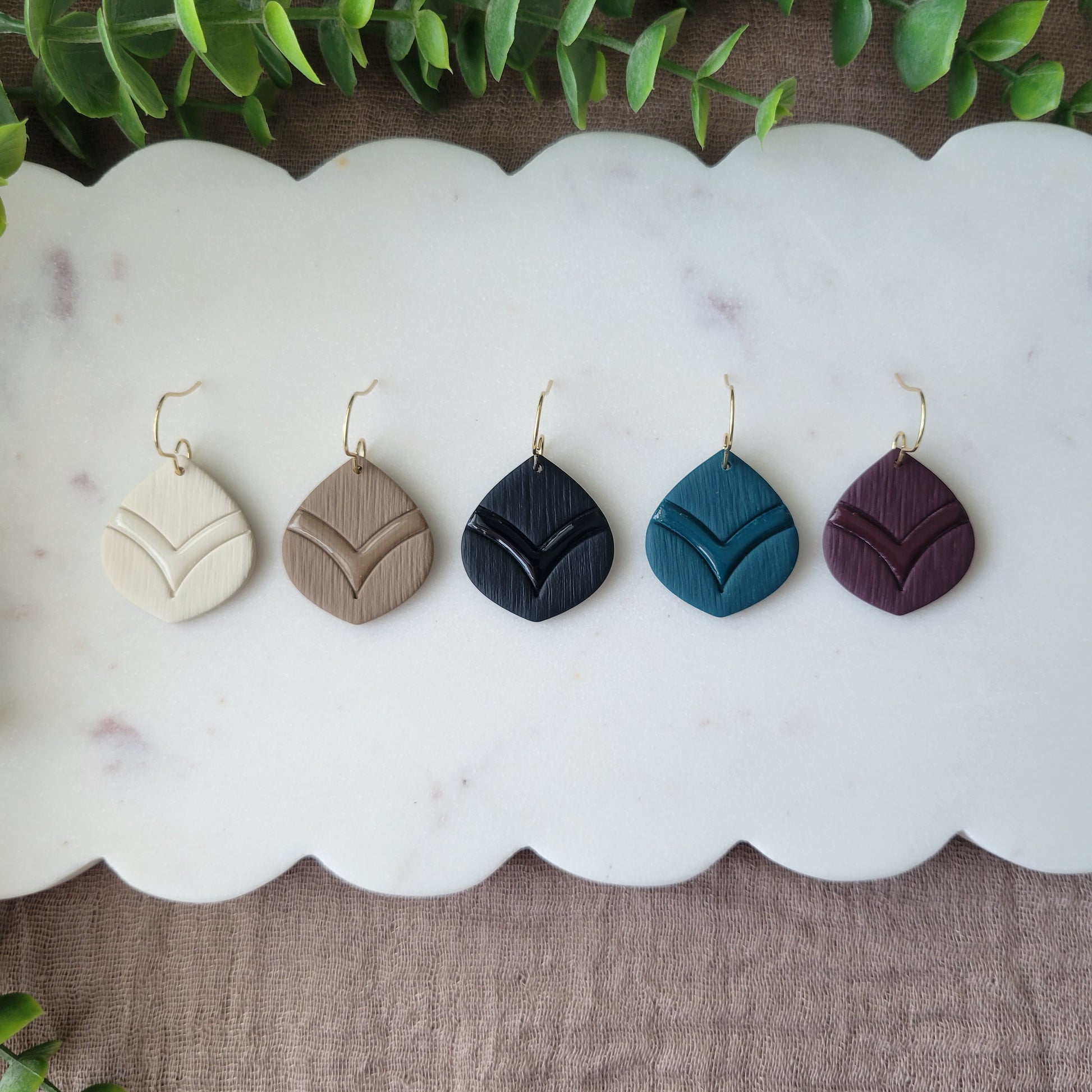 Top view of five round embossed teardrop earrings displayed on a white scalloped tray.