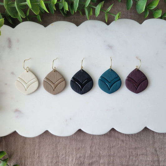 Top view of five round embossed teardrop earrings displayed on a white scalloped tray.