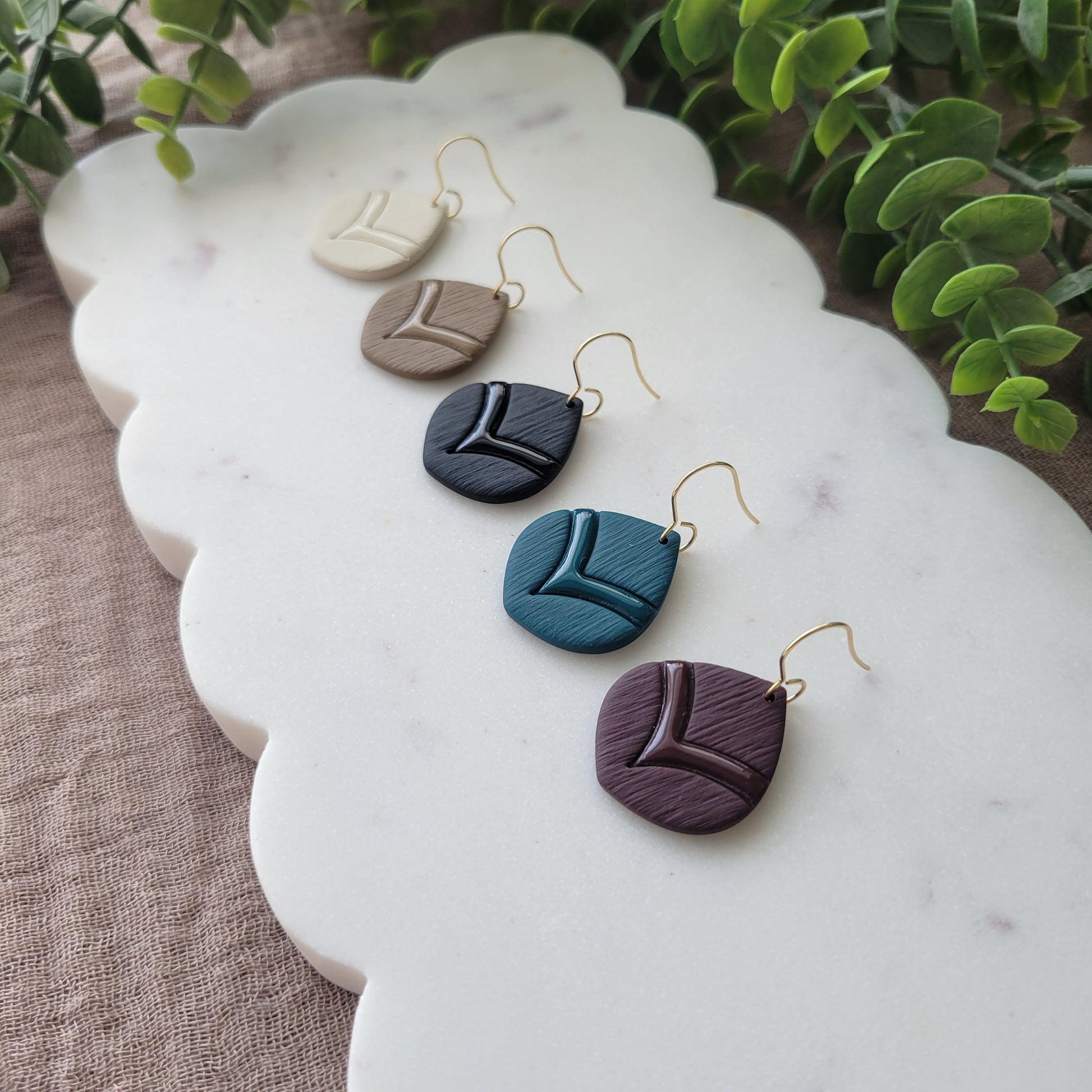 Side view of five round embossed teardrop earrings displayed on a white scalloped tray.