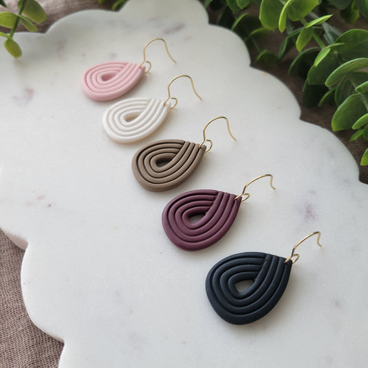 Side view of 5 embossed teardrop earrings displayed on a white scalloped tray.