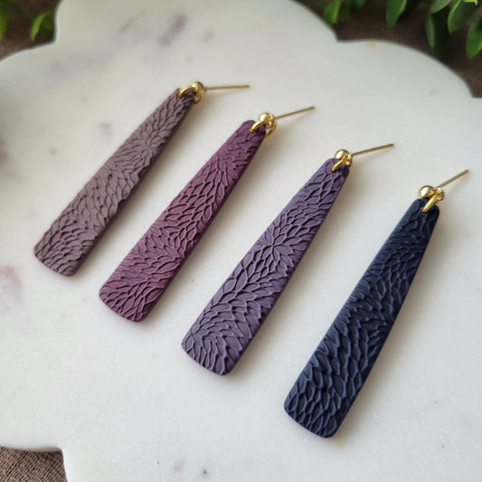 Close up of four pillar earrings with interwoven leaves texture displayed on a white scalloped tray.
