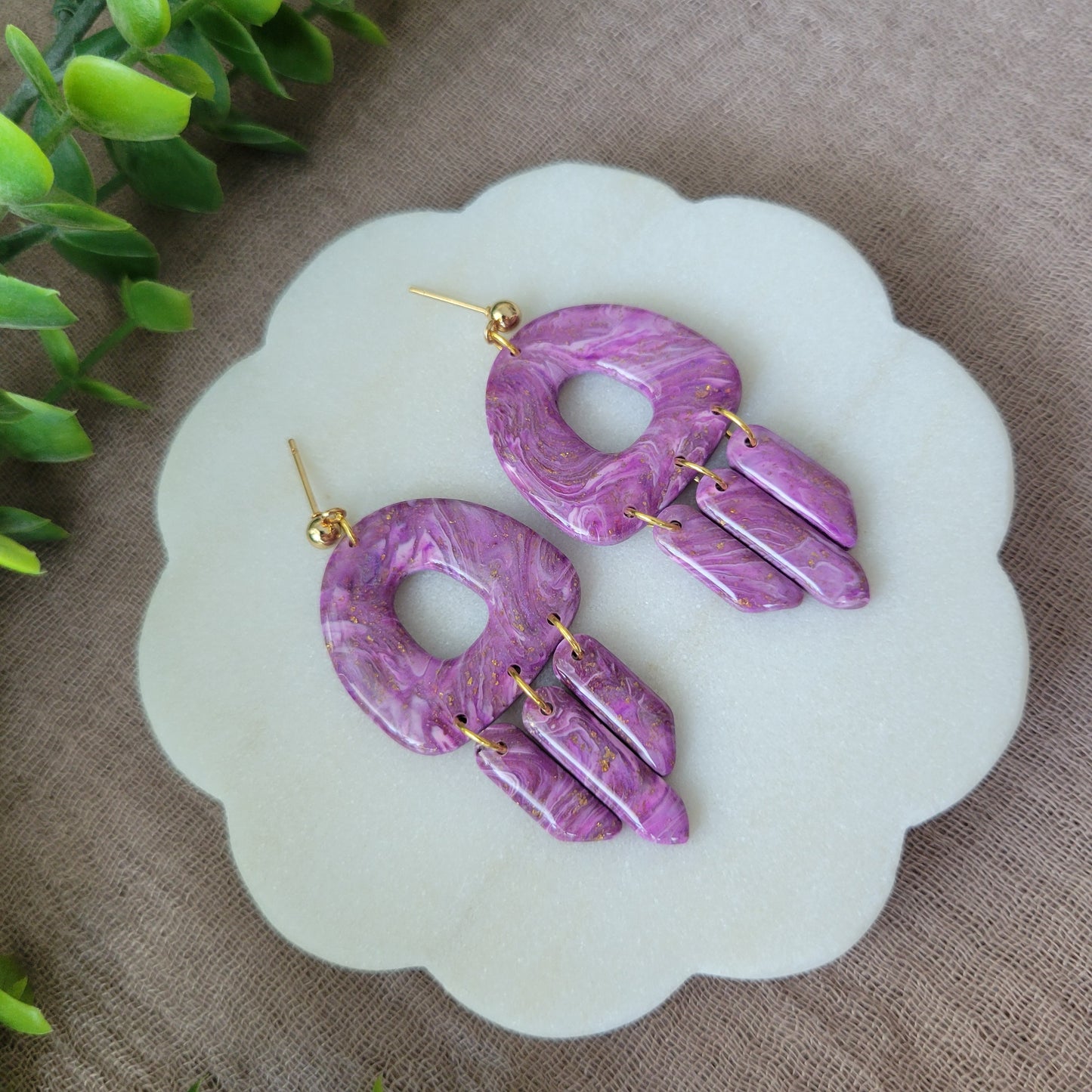 Left side view of a pair of purple marble earrings displayed on a white round scalloped tray.