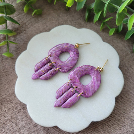 Right side view of a pair of purple marble earrings displayed on a white round scalloped tray.