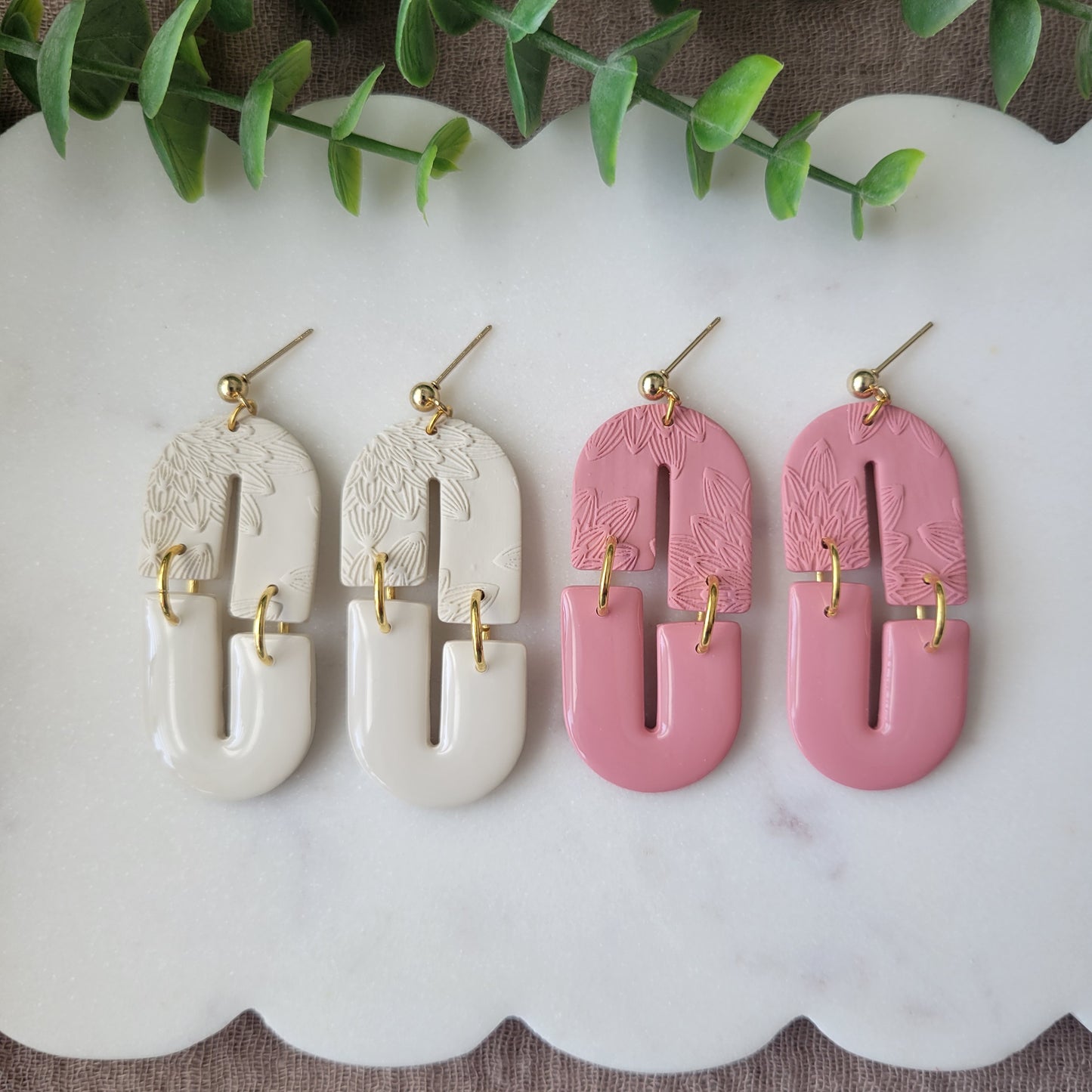 Top view of two pairs of earrings with bloom texture displayed on a white scalloped tray.