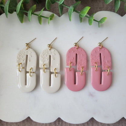 Top view of two pairs of earrings with bloom texture displayed on a white scalloped tray.