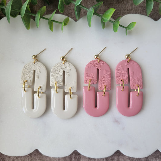 Top view of two pairs of earrings with bloom texture displayed on a white scalloped tray.