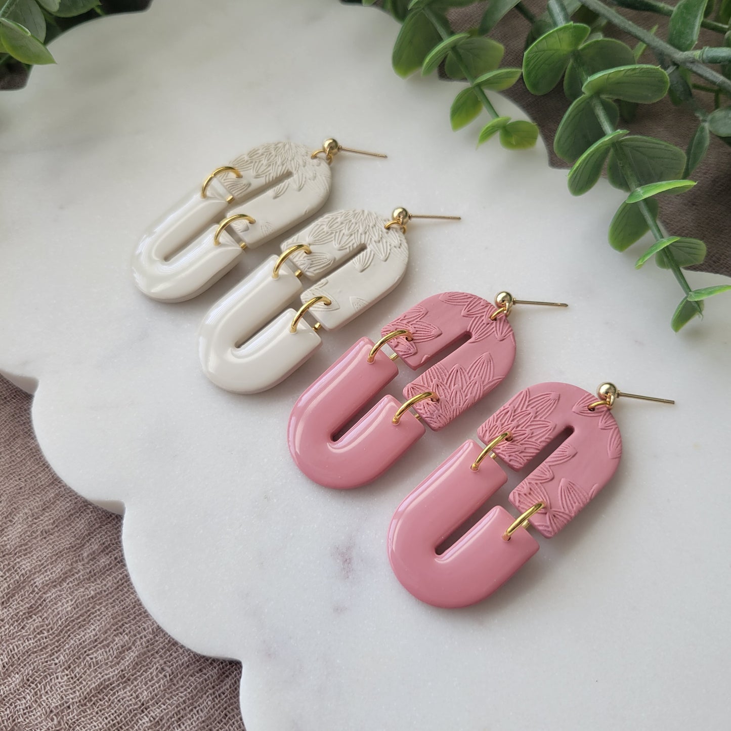 Side view of two pairs of earrings with bloom texture displayed on a white scalloped tray.