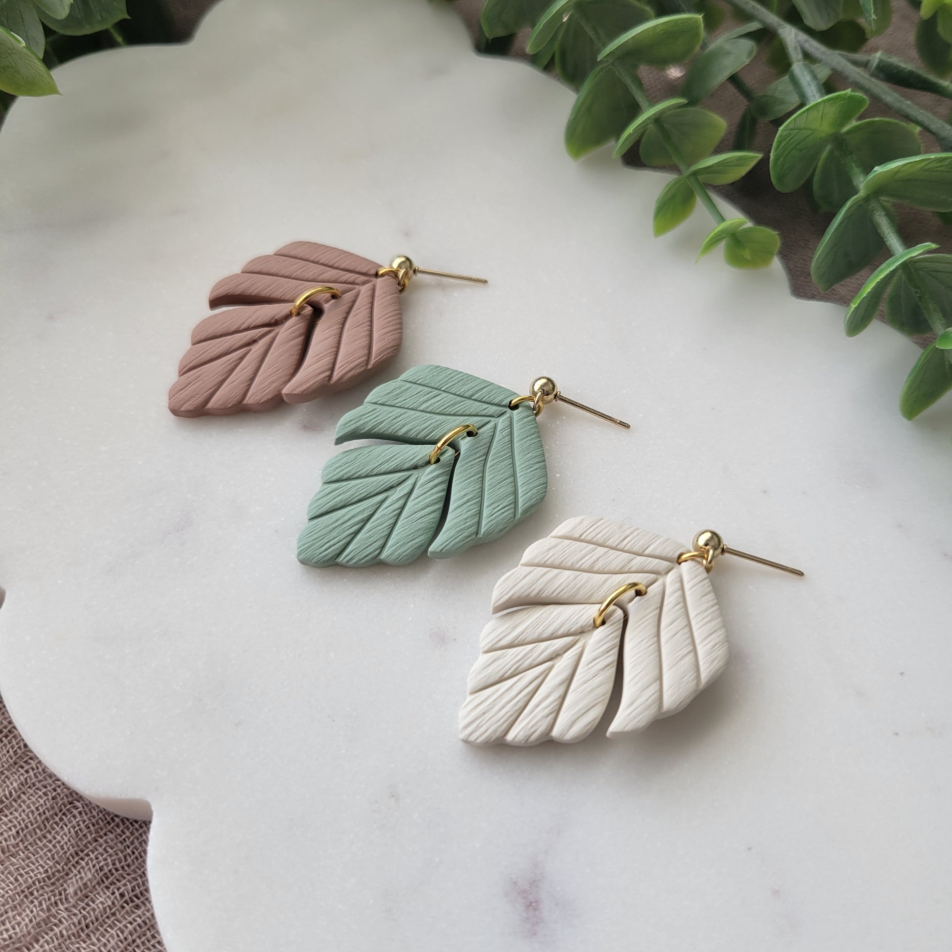 Side view of three leaf shaped earrings displayed on a white scalloped tray.