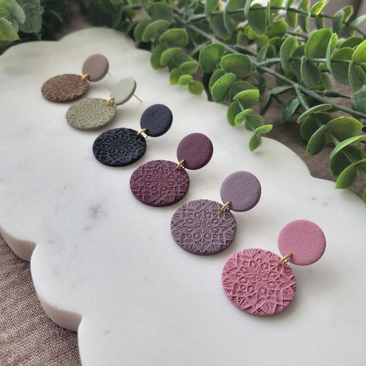 Right side view of six earrings with mandala texture displayed on a white scalloped tray.
