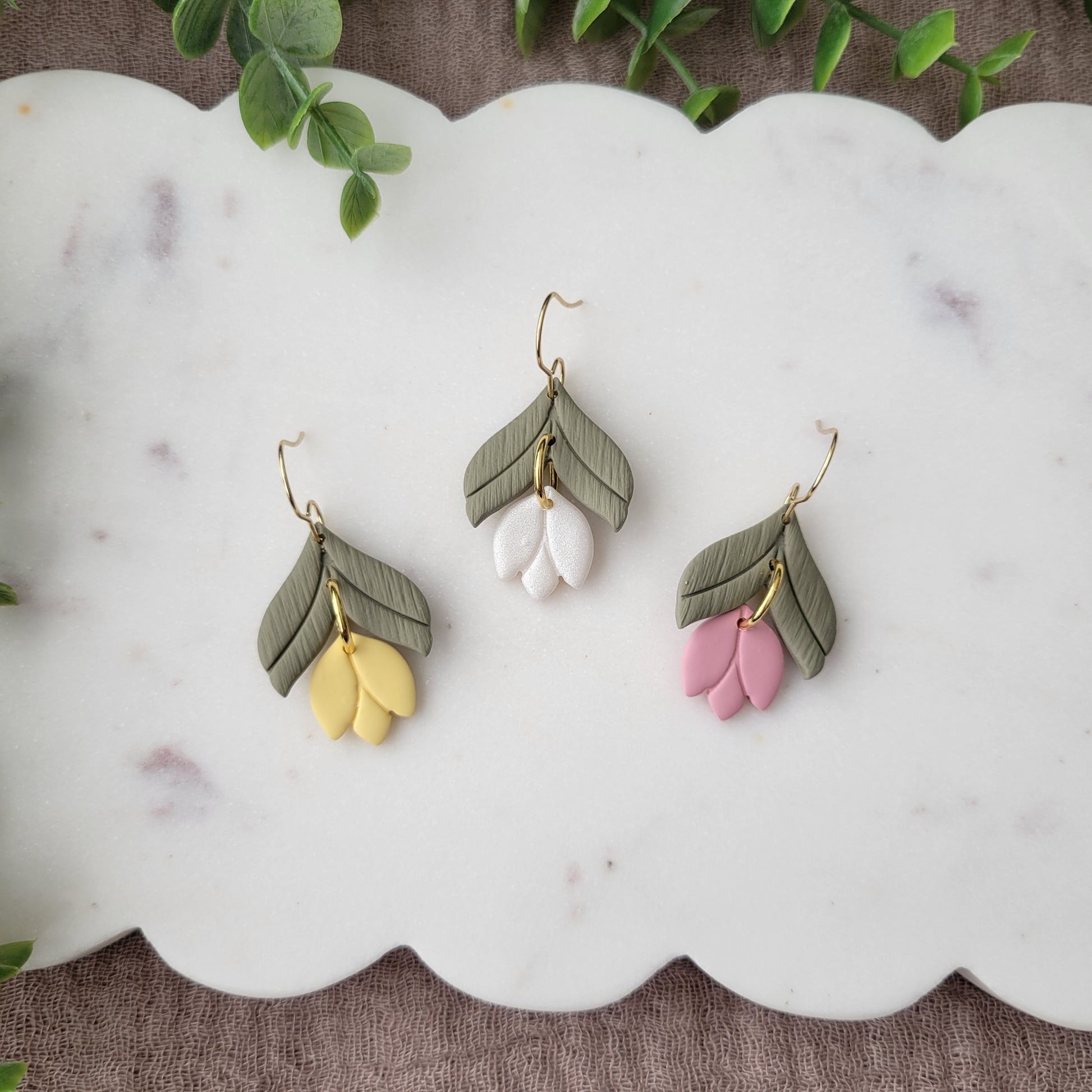 Top view of three tulip shaped earrings displayed on a white scalloped tray.