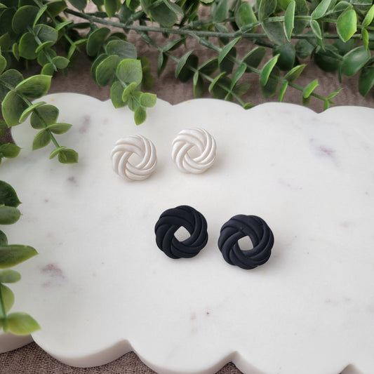 Top view of two pairs of stud knot earrings displayed on a white scalloped tray.