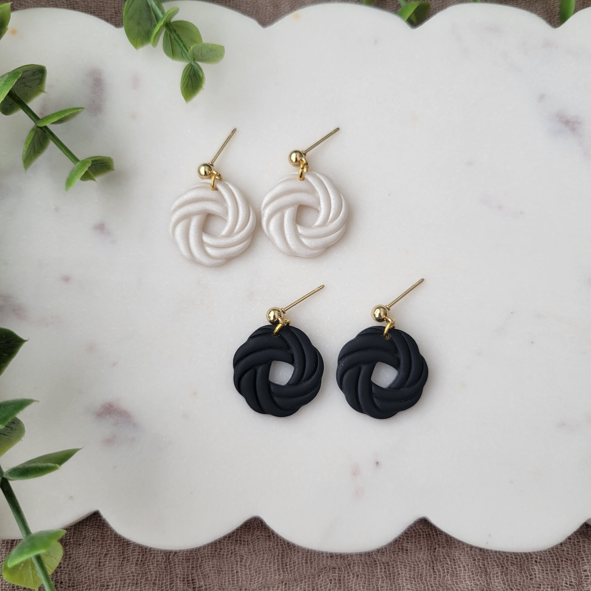 Top view of two pairs of knot dangle earrings displayed on a white scalloped tray.
