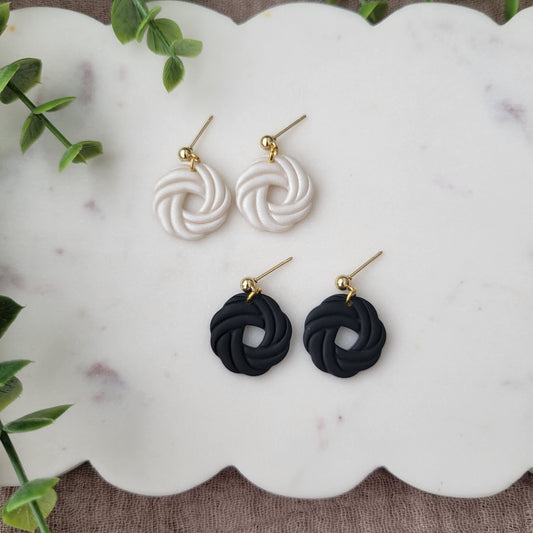 Top view of two pairs of knot dangle earrings displayed on a white scalloped tray.