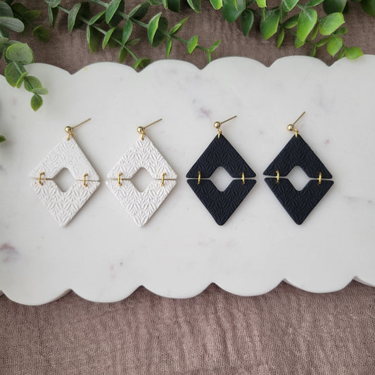 Top view of two pairs of geometric  diamond shaped earrings with art deco flower texture displayed on a white scalloped tray.