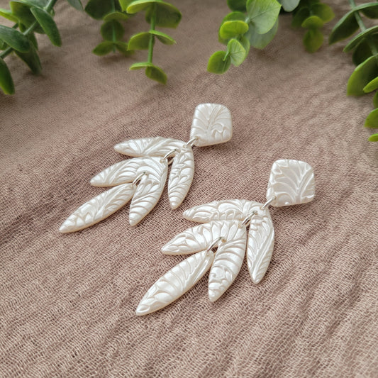 Side view of a pair of pearl long leaf shaped earrings with fancy fern texture displayed on a brown cloth.