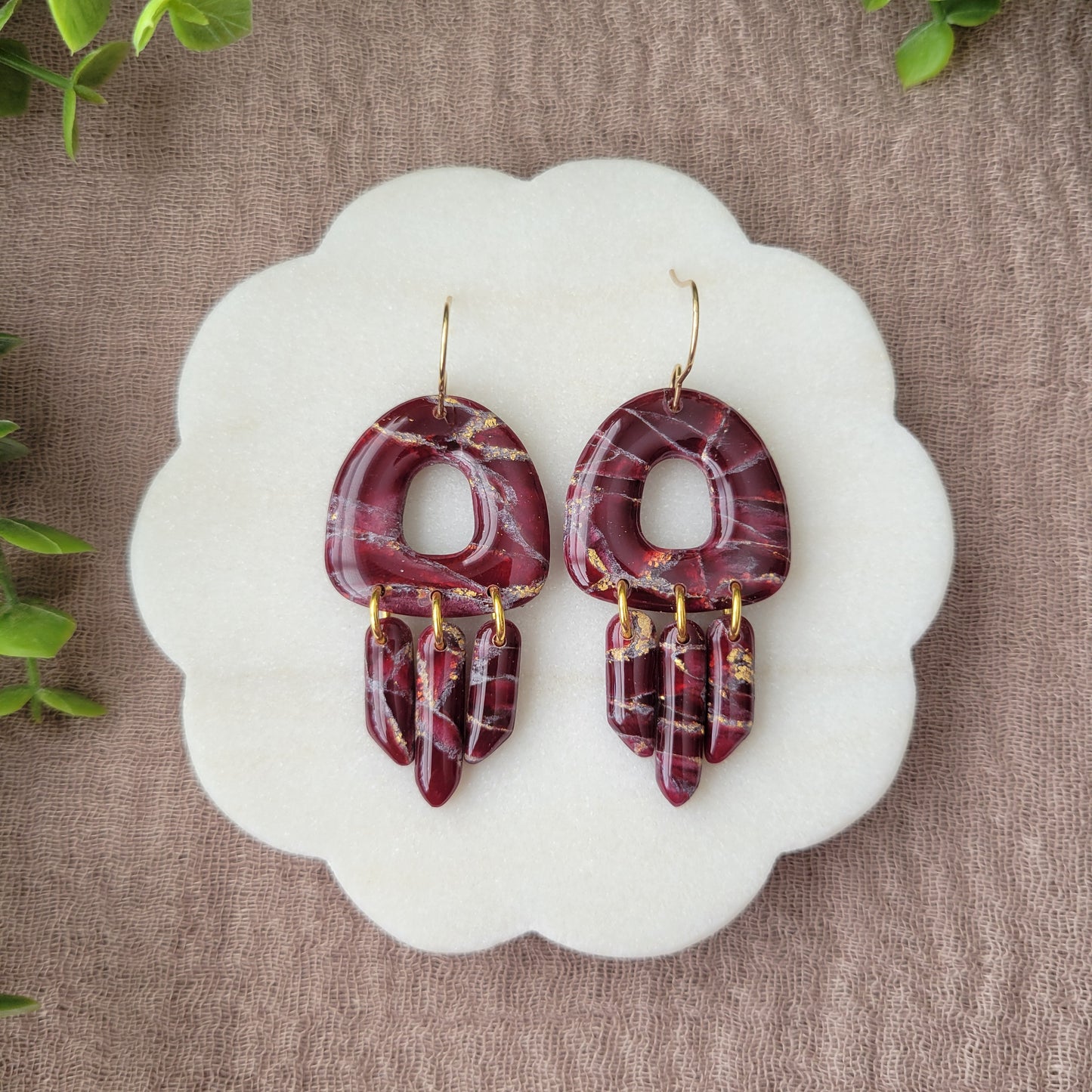 Top view of a pair of Bordeaux colored marble earrings displayed on a white round scalloped tray.