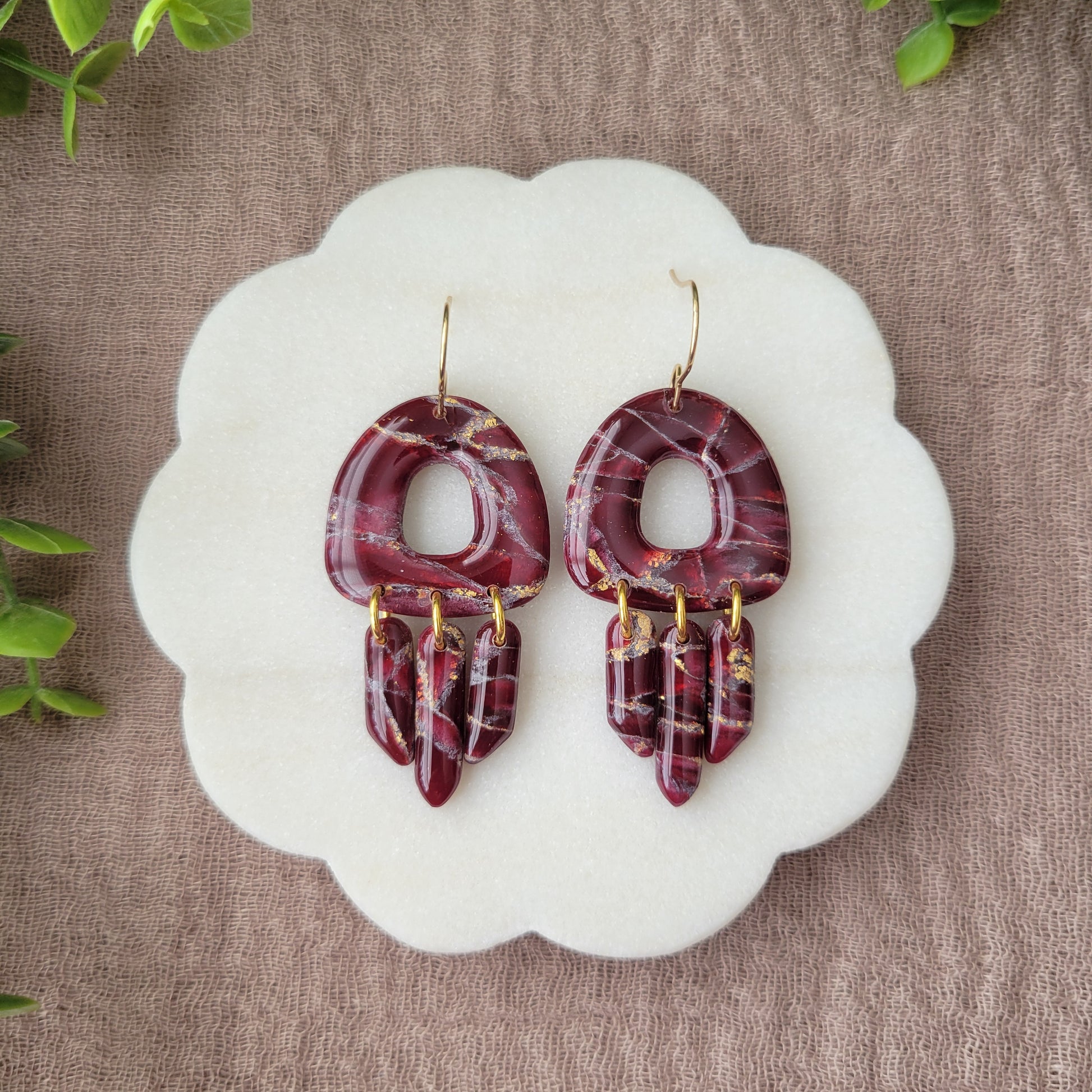 Top view of a pair of Bordeaux colored marble earrings displayed on a white round scalloped tray.