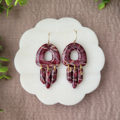 Top view of a pair of Bordeaux colored marble earrings displayed on a white round scalloped tray.