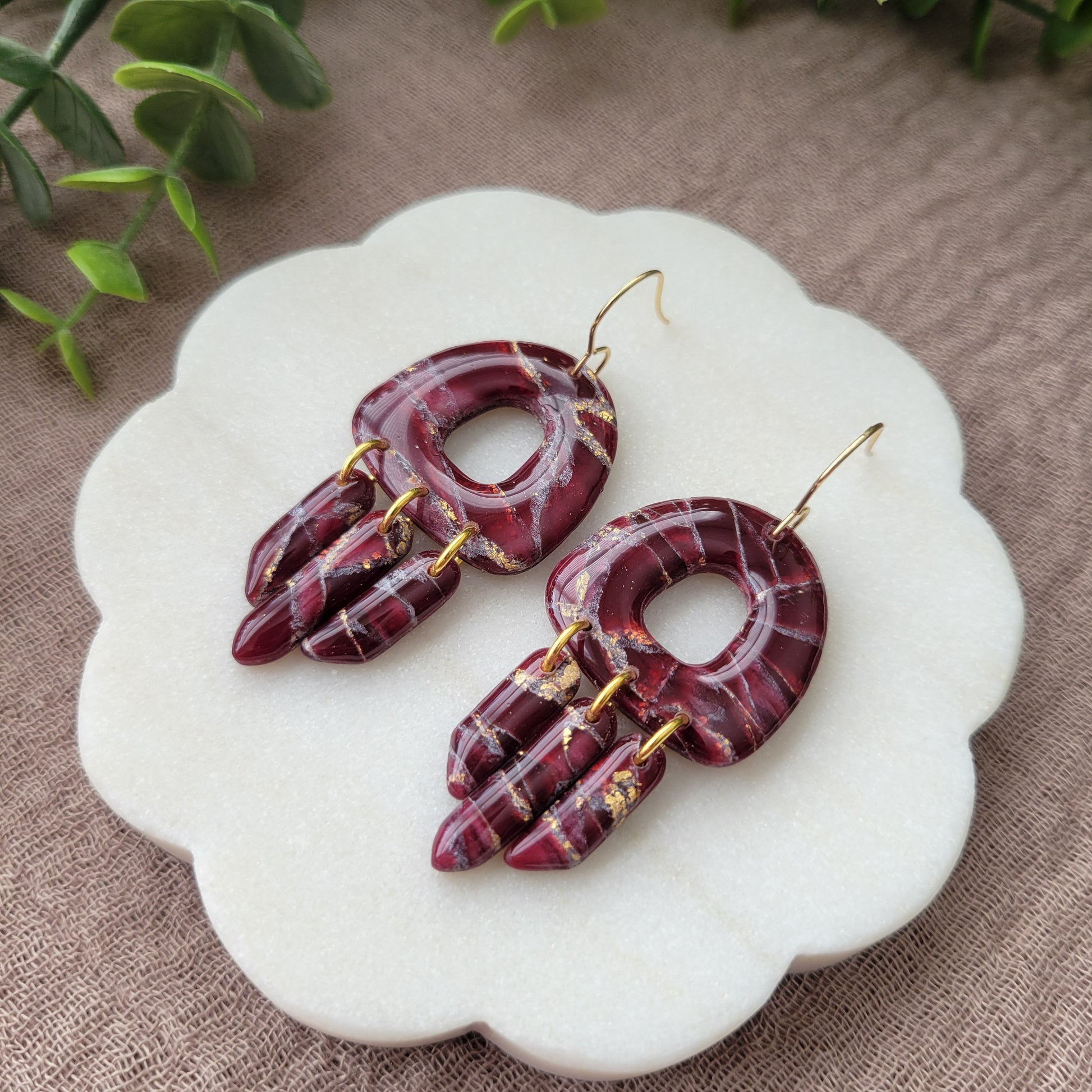 Right side view of a pair of Bordeaux colored marble earrings displayed on a white round scalloped tray.