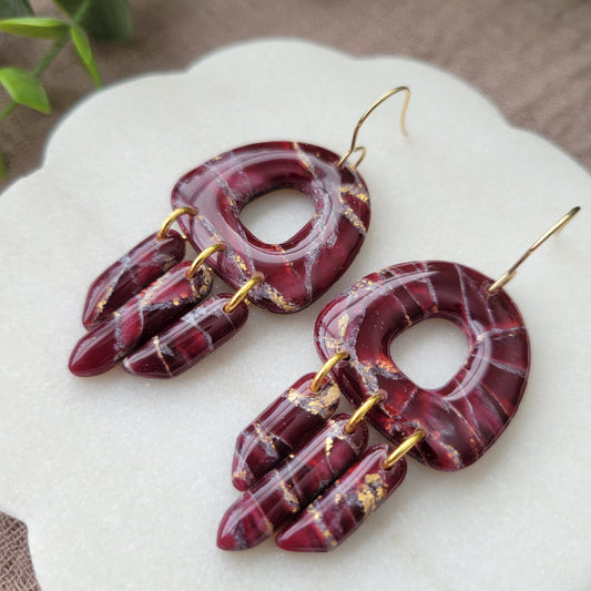 Close up right side view of a pair of Bordeaux colored marble earrings displayed on a white round scalloped tray.