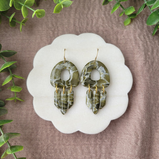 Top view of a pair of green marble earrings displayed on a white round scalloped tray.