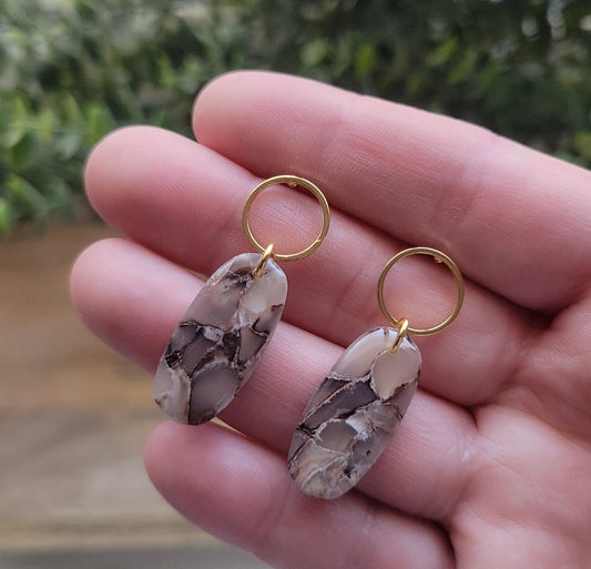 Top view of a pair of brown marble long oval shaped earring displayed on a hand.